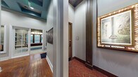 Located at 6650 Corporate Center Pkwy in Jacksonville, Florida, this single-floor amenity center is thoughtfully designed for entertainment and leisure. The entry corridor welcomes visitors with rich hardwood flooring, crisp white trim, and a distinctive teal coffered ceiling accent, setting an elevated tone from the moment of arrival. White-framed French doors with glass panels invite natural light and provide glimpses into adjacent spaces, while tasteful wall art adds a curated, polished aesthetic throughout the hallways.

The centerpiece of the facility is a generously sized private theater room, outfitted with rows of upholstered armchairs and plush sofas arranged to face a large projection screen. Warm amber walls, ornate wall sconces, dark wood architectural columns, and classic movie poster artwork create an immersive, cinema-inspired ambiance. A ceiling-mounted projector completes the full home-theater experience.

Adjacent to the theater is a dedicated game room featuring a full-size billiards table beneath a statement pendant light, a foosball table, and a game table for board games or cards. Cool blue-gray walls, large windows allowing ample natural light, and a wall-mounted television make this space both lively and inviting. Together, these spaces offer a comprehensive and stylish recreational destination.