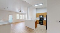 Located in Tempe, Arizona, this two-bedroom, two-bathroom two-story home offers a well-organized layout spread across two floors. The main level features an open-concept kitchen and living area, with light wood-style flooring running throughout. The kitchen is equipped with warm-toned wood cabinetry, white countertops, a breakfast bar peninsula, and black appliances including a range, over-the-range microwave, and refrigerator. The adjoining living area benefits from natural light through multiple windows and includes a ceiling fan overhead. A staircase with clean white railings leads to the upper level, which features vaulted ceilings and a distinctive circular porthole window, adding architectural character. The upper floor houses both bedrooms, including a spacious primary bedroom with a sliding glass door opening to a private balcony with neighborhood views. The primary bathroom features a dual-sink vanity with a wood cabinet base, white countertop, and matte black fixtures. The second bathroom includes a full tub-shower combo. A dedicated walk-in closet with multiple hanging rods and shelving provides generous storage. Light wood-style flooring is consistent throughout both levels, giving the home a cohesive, modern feel.