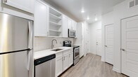 This well-appointed single-floor residence offers a clean, modern aesthetic throughout, combining functional design with contemporary finishes. The open-concept layout seamlessly connects the kitchen and living area, creating a bright and airy atmosphere enhanced by wood-look flooring and a ceiling fan with light fixture.

The kitchen is thoughtfully designed with crisp white shaker cabinetry, open display shelving, a herringbone tile backsplash, quartz countertops, and a full suite of stainless steel appliances including a refrigerator, electric range, microwave, and dishwasher. A large pantry cabinet provides generous storage alongside the well-organized cabinetry.

The living area is open and spacious, bathed in natural light from French doors that lead to a private balcony with outdoor views. The bedroom features plush carpeting, a ceiling fan, and direct access to a generous walk-in closet outfitted with multi-tier wire shelving systems for ample organization.

The bathroom maintains the home's clean, white palette with a shaker-style vanity, quartz countertop, large mirror, and stylish lighting. Built-in open shelving adjacent to the vanity offers convenient storage. Neutral tile flooring ties the space together. Throughout, the unit presents a cohesive, move-in-ready environment with a bright and inviting character.