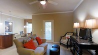 Located at 15 Brasseler Blvd in Savannah, Georgia, this single-floor residence offers a well-appointed and cohesive living environment with a warm, inviting aesthetic throughout. The living area serves as the heart of the home, featuring vaulted ceilings with elegant crown molding that add a sense of height and refinement to the space. A ceiling fan provides both comfort and a classic decorative touch. Natural light filters in through a rear door with a window, brightening the room and creating an airy atmosphere. The living area is open in design, flowing naturally into the dining space, which is illuminated by a stylish pendant light fixture that adds a touch of sophistication. The warm tan wall tones carry consistently throughout, lending the interior a cohesive and welcoming ambiance. The layout is thoughtfully arranged to balance functionality with comfort, providing ample room for seating and everyday living. Overall, this residence combines practical single-floor living with tasteful architectural details, making it a comfortable and well-designed home in the Savannah, Georgia area.