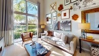 This thoughtfully designed one-bedroom, one-bathroom model unit at 3333 Port Royal Drive in Fort Lauderdale, Florida showcases a contemporary open-concept layout with impressive soaring ceilings that create a striking sense of volume and openness throughout. The kitchen is a standout feature, equipped with stainless steel appliances including a French door refrigerator, microwave, and range, complemented by wood-toned cabinetry that extends to ceiling height, subway tile backsplash, light quartz countertops, and open shelving for display. A freestanding white island provides additional prep and casual dining space. Light-toned large-format tile flooring flows seamlessly throughout the unit. The living room is bathed in natural light from a floor-to-ceiling window that frames lush greenery outside, while a ceiling fan enhances comfort. A curated gallery wall adds artistic character to the space. The bedroom offers a tranquil retreat with natural light from oversized windows, tree-lined views, and thoughtful décor accents. The bathroom features wood-grain cabinetry, a wide vanity with an undermount sink, quartz countertop, a large framed mirror, and a soaking tub, delivering a clean and functional aesthetic throughout.