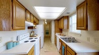 This two-story residence offers a functional and comfortable layout across its two levels. The main living area is open and airy, featuring wall-to-wall plush carpeting that adds warmth underfoot. Tall ceilings enhance the sense of spaciousness, while a window allows natural light to filter in, illuminating the neutral-toned walls. A staircase with carpeted treads leads to the upper floor, providing a clear sense of the home's vertical layout.

The kitchen is designed in a classic galley style, maximizing efficiency with cabinetry lining both sides of the corridor. Warm honey-toned wood cabinets offer generous storage space, complemented by light countertops that provide ample workspace. A double stainless steel sink sits beneath a window, bringing in natural light. The kitchen is equipped with a white electric range and refrigerator, along with a dishwasher. A large skylight panel in the ceiling bathes the kitchen in additional brightness, making it a practical and well-lit space for meal preparation. Tile flooring runs throughout, offering durability and easy maintenance. The overall ambiance of the home is clean, neutral, and move-in ready.