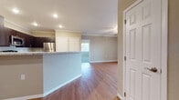 This single-floor residence offers a thoughtfully designed open-concept layout that seamlessly connects the kitchen and living areas. The kitchen is a standout feature, equipped with dark espresso cabinetry, granite-style countertops, and a full suite of stainless steel appliances including a range, over-the-range microwave, and refrigerator. A peninsula with a matching countertop provides a natural divider between the kitchen and the expansive living area, which is finished with warm wood-style flooring and recessed lighting throughout. Crown molding adds a polished architectural detail to the main living spaces. The bedrooms offer a comfortable retreat; the primary bedroom includes access to a generously sized walk-in closet fitted with dual hanging rods and extensive built-in shelving, while secondary bedrooms feature plush carpeting and standard closets. The primary bathroom is appointed with a dual-sink vanity topped with granite-style countertops, dark wood cabinetry, and a tub-shower combination. A secondary bathroom mirrors the same refined finishes with a single-sink vanity. Natural light filters into the living area through a window, contributing to the overall bright and welcoming ambiance of the home.
