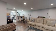 Located at 126 New Britain Ave in Plainville, CT, this single-floor unit offers a well-designed layout with a cohesive, modern aesthetic throughout. The open-concept living and dining area is anchored by rich hardwood-style flooring, recessed lighting, and a bright, neutral color palette. The living room provides comfortable space for relaxing, with a large window allowing natural light to filter in alongside a wall-mounted HVAC unit. A dining area with pendant lighting sits seamlessly between the living space and the kitchen, creating an inviting flow for everyday living and entertaining.

The kitchen is a standout feature, outfitted with white shaker-style cabinetry accented by gold hardware and dark upper trim. Stainless steel appliances — including a range, microwave, dishwasher, and refrigerator — complement the classic white subway tile backsplash and light tile flooring.

The primary bedroom features warm hardwood-style floors, a bold accent wall in deep gray-blue, natural window light, and a stylish sputnik-style ceiling fixture. A second bedroom offers the same flooring and a clean, functional layout. The bathroom is neatly appointed with a white vanity and a shower-tub combination dressed with a decorative curtain, maintaining the unit's clean, contemporary feel throughout.