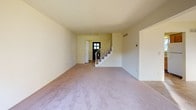 This three-floor townhome in Ann Arbor, Michigan offers a practical and well-distributed layout across its levels. The main living area features neutral-toned carpet, a ceiling fan, and a sliding glass door that opens directly to a green outdoor space, allowing generous natural light to fill the room. A staircase with decorative railings connects the main level to the upper floor, and a separate entry door with a windowed panel provides a welcoming foyer.

The galley-style kitchen is equipped with warm oak cabinetry, a white range, a black dishwasher, and a double sink beneath a window. Tile flooring runs throughout the kitchen and connects to an adjacent dining or pass-through area with additional natural light.

Upstairs, the bedrooms are carpeted and bright, with windows offering views of the surrounding neighborhood. The full bathroom on this level includes a white vanity with under-cabinet storage, a multi-bulb light fixture, dual mirrors, and tile flooring. A half bathroom on another level features a single-sink vanity, toilet, and a large window.

The unfinished basement provides significant bonus space with carpeted flooring, exposed joists, ductwork, small ground-level windows, and utility systems, offering potential for storage or future customization.