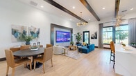 Located at Bay Island Lane in Kindred, Florida, this thoughtfully designed single-story community space offers a generous and versatile layout across a single level. The interior is anchored by a contemporary aesthetic, combining light hardwood flooring, teal accent ceilings, bold black-framed glass partitions, and crisp white walls throughout.

The two living areas serve distinct purposes — one is a relaxed lounge with statement velvet blue seating, a large-format display wall, exposed wood beam ceilings, and a striking sputnik-style chandelier. The other is a bright, open gathering area flooded with natural light, featuring tray ceilings finished in teal and pendant lighting over a built-in bar counter with seating.

The kitchen area is appointed with quartz countertops, a stainless undermount sink, an intricate fish-scale tile backsplash, and gold-toned hardware, with views of a lushly landscaped exterior courtyard featuring palm trees.

The dining room and office spaces offer flexible meeting configurations, each featuring large windows with outdoor views of the Florida landscape, warm leather seating, and modern pendant lighting. Floor-to-ceiling black-framed glass walls provide both openness and privacy.

Throughout, the space exudes a polished, resort-inspired ambiance with curated artwork, layered textures, and abundant natural light — ideal for community gathering and collaboration.
