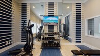 Located in Columbia, Tennessee, this fitness center is a thoughtfully designed space built to support a comprehensive workout experience. The room features a striking navy blue and white striped wall treatment with decorative horizontal slat panels that give the space a modern, polished aesthetic. Full-length mirrors are strategically placed throughout, visually expanding the room and allowing users to monitor their form during exercise.

The flooring combines light hardwood with blue rubberized mat sections, offering both durability and comfort across different workout zones. Natural light filters in through large windows fitted with white blinds, creating a bright and energizing atmosphere complemented by recessed ceiling lighting.

The space is outfitted with a well-rounded selection of fitness equipment, including SportsArt treadmills and elliptical trainers for cardiovascular conditioning. A multi-functional cable machine anchors the strength training area, while a full rack of dumbbells spanning a wide weight range provides options for free weight workouts. An adjustable workout bench adds further versatility. A wall-mounted flat-screen television enhances the experience during cardio sessions. The overall ambiance is clean, functional, and motivating — a professional-grade fitness facility designed to meet a variety of fitness needs.