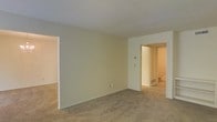 This three-floor property offers a straightforward, functional layout with a clean and neutral aesthetic throughout. The main living area shown features wall-to-wall carpeting in a warm beige tone, complemented by cream-colored walls that create a bright, understated atmosphere. The smooth white ceiling adds to the sense of openness in the space.

The room benefits from an open-plan design, with a visible passageway connecting to adjacent areas, including what appears to be a hallway leading to a staircase accessing the additional floors. This layout promotes easy flow and connectivity between the living spaces. A thermostat is mounted on the wall, and a floor vent indicates a central heating and cooling system throughout the property.

The neutral color palette across the floors provides a versatile backdrop, suitable for a variety of furnishing styles. The carpeted flooring adds warmth and comfort underfoot, while the clean lines of the architecture maintain a simple, uncluttered look. With three floors of living space, this property offers ample room across multiple levels, making it well-suited for those seeking a spacious, multi-story home environment.