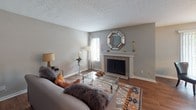 Located in the Pleasant Lake Village community of Duluth, Georgia, this single-floor residence offers a thoughtfully designed layout with warm, neutral tones and hardwood-style flooring throughout. The living room serves as an inviting focal point, anchored by a classic fireplace with a tile surround and white mantel, complemented by natural light filtering through windows with blinds. The kitchen is outfitted with rich dark wood cabinetry, light countertops, and black appliances, providing ample storage and prep space in an efficient layout. The primary bedroom is generously proportioned, featuring large windows with drape panels that invite natural light, hardwood-style flooring, and tasteful decor accents. A second bedroom offers a cozy, well-styled retreat with warm lighting and decorative wall art. The bathrooms are finished in clean whites, with one featuring a single vanity with light countertops and bright overhead lighting, and another offering a full tub-shower combo with louvered closet doors providing additional storage. The overall ambiance of the home is warm and comfortable, with consistent neutral grey wall tones and classic finishes that create a cohesive and inviting atmosphere throughout.