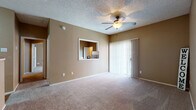 This single-floor residence is thoughtfully laid out to maximize comfort and functionality throughout. The open living area serves as the heart of the home, featuring warm beige walls, plush wall-to-wall carpeting, and a ceiling fan with integrated lighting. A sliding glass door with vertical blinds leads to an outdoor area, allowing natural light to fill the space. A convenient pass-through window connects the living area to the kitchen, enhancing the open feel between the two spaces.

The kitchen is equipped with white cabinetry, granite-style countertops, a double-basin stainless steel sink, and black appliances including a range and overhead microwave. Wood-style flooring and a pendant light fixture complete the kitchen's practical yet inviting character.

The bedrooms continue the warm, neutral aesthetic with soft carpeting, ceiling fans, and ample natural light from horizontal-blind-fitted windows. Each bedroom includes access to a walk-in or reach-in closet for generous storage.

The bathroom features white cabinetry with a granite-style countertop, a large vanity mirror, and a tub and shower combination. A textured ceiling is consistent throughout the unit, adding a classic residential finish to every room.