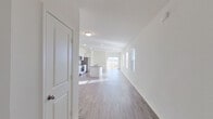 This single-story home is designed with a clean, contemporary aesthetic characterized by crisp white walls, recessed lighting, and wood-look flooring that runs throughout the main living areas. The open-concept floor plan connects the living area to the kitchen and dining space seamlessly, creating a generous, light-filled environment enhanced by natural light streaming through multiple windows and a sliding glass door at the rear of the home.

The kitchen is well-equipped with white shaker-style cabinetry, granite countertops, and a full suite of stainless steel appliances, including a refrigerator, range, and microwave. A central island provides additional prep and dining space, reinforcing the kitchen's functional design.

Two bathrooms serve the home: a primary bathroom featuring a walk-in shower with sliding glass doors and a white vanity, and a secondary bathroom equipped with a tub-shower combination. Both bathrooms include wood-look flooring and white cabinetry for a cohesive finish.

Additional highlights include a dedicated laundry room with wire shelving and utility hookups, as well as a carpeted walk-in closet outfitted with wire shelving systems. Throughout, the home maintains a neutral, move-in-ready palette.