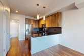 Located in Seattle's Lower Queen Anne neighborhood, this one-bedroom, one-bathroom residence offers a well-designed layout across a single floor. The open-concept living, dining, and kitchen area serves as the heart of the home, showcasing warm hardwood flooring throughout. The kitchen is a standout feature, equipped with stainless steel appliances including a range, microwave, and French door refrigerator. Rich wood cabinetry contrasts beautifully with dark countertops and a slate-blue subway tile backsplash, while pendant lighting adds a modern finishing touch. A peninsula with additional counter space creates a natural divide between the kitchen and living area. The bedroom is carpeted for comfort, features a ceiling fan, and is bathed in natural light through a large window with city views. A dedicated walk-in closet provides generous storage. An additional den offers flexible space for a home office or guest area. The full bathroom is finished with large-format tile flooring, a wood-toned vanity with white countertop, a full mirror, and a tub-shower combination with crisp white tile surround.