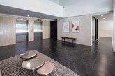 Located at 30 Edith Dr in Toronto's midtown neighbourhood, this single-floor amenity space presents a refined and contemporary design aesthetic throughout. The grand entrance lobby immediately impresses with its soaring double-height ceiling, dark marble-effect tile flooring, and generous glazed double doors that flood the space with natural light and offer views of the surrounding greenery. A sleek wooden bench and carefully selected framed line-art pieces lend the entry a gallery-like quality.

The central lounge area serves as the heart of the space, anchored by a warm caramel-toned sofa set atop a textured area rug, complemented by a cluster of round nesting tables. Above, an eye-catching arrangement of sculptural pendant lights in muted, multicoloured tones adds an artistic focal point to the high ceiling. The pale stone-clad walls and dark marble flooring create a sophisticated contrast throughout.

A more intimate seating nook features stylish pendant lighting, a marble-top bistro table, and woven accent chairs, ideal for casual conversation or quiet moments. The adjacent meeting room is bright and functional, equipped with a long wooden conference table and green upholstered chairs, all bathed in natural light through expansive floor-to-ceiling sliding glass doors that open to outdoor views — completing a polished and welcoming communal environment.