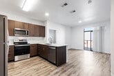 This contemporary single-floor residence is designed with a clean, modern aesthetic and a thoughtful, functional layout. The open-concept kitchen and living area serves as the heart of the unit, where rich dark-wood laminate cabinetry contrasts beautifully with light quartz countertops. The kitchen is fully equipped with stainless steel appliances, including an electric range, over-the-range microwave, and dishwasher, alongside a peninsula with an undermount sink — ideal for both meal preparation and casual dining. Recessed lighting and a skylight-style fixture keep the space bright and welcoming. Light wood-look luxury vinyl plank flooring runs consistently throughout the entire unit, adding warmth and cohesion to every room. The living area flows seamlessly toward a full-width sliding glass door that opens onto a private balcony, offering natural light and outdoor views. The bedroom is a calm, well-proportioned space featuring a large window with horizontal blinds that filters natural light while maintaining privacy. The bathroom is clean and efficiently designed, featuring a soaking tub with a shower surround, light wood-look flooring, a dark-wood vanity with a white countertop, and brushed nickel fixtures. A dedicated in-unit laundry area adds further convenience. The overall ambiance is fresh, contemporary, and move-in ready.