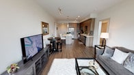 This thoughtfully designed single-floor residence combines contemporary style with functional living. The open-concept layout connects the living area to the kitchen seamlessly, with warm hardwood-style flooring running throughout the main space. The living area features track lighting, a glass-top coffee table, and access to a private balcony that brings in natural light.

The kitchen is well-appointed with wood-grain cabinetry extending to the ceiling, stainless steel appliances including a gas range, built-in microwave, dishwasher, and a French door refrigerator. A subway tile backsplash in a soft gray-blue tone adds texture, while the white countertops provide a clean contrast. A separate kitchen island with seating offers additional prep and dining space.

Both bedrooms are comfortably sized, each featuring a ceiling fan, neutral carpeting, and dedicated walk-in closets with built-in shelving and hanging rods. The primary bedroom benefits from a large window with outdoor views, enhancing the sense of openness.

Two bathrooms serve the residence. One features a walk-in glass-enclosed shower with recessed shelving and a backlit vanity mirror. The second includes a combination tub and shower with the same modern vanity styling, maintaining a cohesive aesthetic throughout.