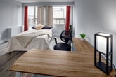 Located on the third floor at 186 King Street in downtown London, Ontario, this efficiently designed unit offers a thoughtful open-concept layout that maximizes every square foot. Light-toned laminate hardwood flooring runs throughout the main living area, contributing to a clean, cohesive aesthetic anchored by white walls and white trim.

The primary living and sleeping area is generously proportioned relative to the unit's overall footprint, accommodating a full-sized bed alongside a dedicated workspace. A large window with floor-to-ceiling curtain panels allows considerable natural light to filter in while offering views of the surrounding cityscape. The open layout allows for flexible furniture arrangements to suit both living and working needs.

The kitchen occupies a defined corner of the main space and features white cabinetry extending to the ceiling, a stainless steel refrigerator, a gas range, and a single-basin sink — providing full cooking functionality within a compact footprint. A sliding door separates the entry corridor from the main room, enhancing privacy.

The bathroom is finished with neutral tile flooring, a white vanity with a stone-look countertop, and a shower-tub combination, maintaining the unit's clean, minimal palette throughout.