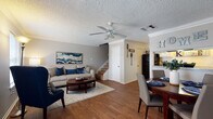 This two-story residence offers a thoughtfully designed layout that balances comfort and functionality. The main floor features an open-concept living and dining area connected by rich hardwood-style flooring throughout. The living room is anchored by a ceiling fan, crown molding, and a textured ceiling, creating a warm and welcoming atmosphere. A staircase leads to the upper level, while the dining area sits adjacent to a pass-through opening that connects to the galley-style kitchen. The kitchen is outfitted with white cabinetry, granite-look countertops, a double sink, and black appliances, providing ample workspace in an efficient layout. A half bathroom on the main level features a granite-topped vanity with white cabinetry. Upstairs, the carpeted bedrooms offer a quieter retreat, each with crown molding, textured ceilings, and natural light from window treatments. One bedroom features neutral tones with a side window, while the second presents a cozy, well-proportioned layout. The upper hallway connects the bedrooms with ease. Throughout the home, a consistent neutral color palette and crown molding details lend a cohesive, polished character to every room.