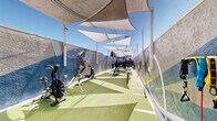 Located at 678 Bellflower Ave in Sunnyvale, California, this open-air fitness facility offers a dynamic and purpose-built training environment under the sunny Bay Area sky. The elongated layout is covered by a series of large triangular shade sails that provide relief from direct sunlight while keeping the space fully open to fresh air and natural light.

The entire floor is surfaced with artificial turf marked with training lines, creating a clean, functional space ideal for a variety of athletic activities. Bold, large-scale athletic murals adorn the perimeter walls, featuring dynamic imagery of athletes in motion, giving the space an energetic and motivating ambiance.

The facility is well-equipped for functional and high-intensity training. A central rack houses an array of medicine balls and battle ropes, while air bikes and rowing machines are positioned along one side for cardio conditioning. A heavy tire and sled station, a flat weight bench, and a rope climb anchor round out the training zones. String lights are strung overhead near the entrance gate, adding a welcoming touch during evening hours.

The space is enclosed by solid perimeter walls and a wooden gate, ensuring a focused and private training atmosphere. Designed for performance and community fitness, this outdoor gym delivers a compelling and well-organized workout experience.