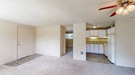 This single-floor unit offers a practical and efficient layout across three bedrooms, one bathroom, and a kitchen. The living area features neutral-toned carpet, vertical wood panel wall accents, and a textured popcorn ceiling. A ceiling fan with a light fixture provides overhead airflow, while a sliding glass door opens to an outdoor space, allowing natural light to fill the room and offering views of the surrounding exterior.

The kitchen is neatly appointed with white cabinetry extending to the ceiling, a countertop with a built-in sink, a range, and a full-size refrigerator. Light wood-look flooring grounds the space and transitions into the carpeted areas of the unit. The open layout between the kitchen and living area provides a cohesive flow throughout the common spaces.

Each bedroom is carpeted and features textured ceilings, with windows that bring in natural light and views of greenery. One bedroom includes a sliding closet with wood-paneled interior detailing. The primary bedroom is notably spacious, featuring a ceiling fan, a sliding glass door, and an additional window for cross-ventilation and abundant light.

The bathroom includes a full tub and shower combo, fully tiled in neutral beige square tiles with chrome fixtures, complemented by a toilet and vanity.