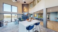 Located at 260 Rim View Dr in Colorado Springs, CO, this single-floor community clubhouse offers a thoughtfully designed gathering space that blends contemporary style with functional amenities. The centerpiece of the space is a dramatic great room with soaring double-height ceilings and oversized clerestory windows that flood the interior with abundant natural light. A striking floor-to-ceiling textured fireplace wall anchors the lounge area, complemented by modern pendant lighting and a large mounted TV. Sliding glass doors open directly to an outdoor area, framing scenic Colorado views and seamlessly connecting the interior to the outdoors. A substantial white island with bar seating serves as the social hub between the lounge and the dining zone, where a long communal table and coordinating blue chairs provide ample seating for gatherings. The adjacent kitchenette features light wood-toned countertops, white cabinetry, pendant lighting, and a pass-through window. Warm hardwood-style flooring runs throughout much of the space, transitioning to plush area rugs in the lounge. The overall design palette of teal, slate blue, warm amber, and crisp white creates a vibrant yet cohesive modern aesthetic throughout.