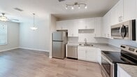 Located at 2745 Red Apple Circle in Kissimmee, FL, this one-bedroom, one-bathroom unit offers a well-designed, single-floor layout making efficient use of its space. The open-concept living and kitchen area features wood-look luxury vinyl flooring, creating a clean and cohesive feel throughout. The kitchen is outfitted with white shaker-style cabinetry, granite-look countertops, a stainless steel refrigerator, dishwasher, microwave, and electric range, along with track lighting and a pendant light that illuminate the space effectively. A dedicated in-unit laundry area accommodates a full-size washer and dryer, adding practical convenience. The bedroom is generously proportioned, finished with plush carpet, a ceiling fan, and two windows dressed with faux-wood blinds that allow natural light while offering views of the surrounding community. The bedroom also includes a closet and direct access to the bathroom. The bathroom is clean and functional, featuring a tiled tub-shower combination, wood-look flooring, and neutral wall tones. Throughout the unit, neutral paint tones and recessed lighting contribute to a bright, welcoming ambiance suitable for comfortable everyday living.