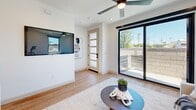 This contemporary two-story home in Phoenix, AZ offers a thoughtfully designed layout spread across two levels. The ground floor houses an attached garage with epoxy-coated flooring and a windowed panel door, providing secure and functional parking. The upper level opens into a bright, open-concept living and kitchen area bathed in natural light, featuring light hardwood flooring and ceiling fans throughout. Large black-framed sliding glass doors connect the living room to an outdoor balcony, while a frosted-panel entry door adds a modern touch. The kitchen is a standout, boasting a two-tone design with white upper cabinetry, warm wood lower cabinets, a white quartz island, subway tile backsplash, stainless steel appliances, and gold-accented hardware. The primary bedroom is generously sized, featuring expansive black-framed windows that flood the room with natural light and offer open views of the surrounding neighborhood. The bathrooms are elegantly finished with marble-style tile flooring, white subway tile surrounds, and brushed gold fixtures. A dedicated closet and hallway provide practical storage and circulation. Clean white walls, recessed lighting, and consistent hardwood flooring unify the home's modern, minimalist aesthetic throughout.