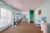 Located at 17040 Frances St in Omaha, Nebraska, this fitness center offers a generously sized, single-floor layout designed to support a comprehensive workout experience. The main exercise room is the heart of the space, painted in a bright aqua-green palette that creates an energizing and welcoming atmosphere. Carpet flooring runs throughout, providing comfort underfoot across the workout areas.

The cardio zone features a row of True-brand treadmills and an elliptical trainer, each positioned in front of wall-mounted flat-screen televisions for an engaging workout experience. Ceiling fans are installed overhead to promote airflow and comfort during exercise sessions.

The strength training area is well-appointed with a power rack, cable machines, selectorized weight machines, and a full dumbbell rack, accommodating a wide range of resistance training routines. Large windows along the walls allow natural light to fill the space and provide views of the surrounding outdoor greenery. Full-length mirrors are strategically placed to assist with form and to amplify the sense of openness.

A water cooler station and storage shelving are available for convenience. A connecting hallway provides access between sections of the facility. Recessed lighting throughout ensures the space remains bright and functional at all times.