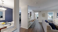 This 2-bedroom, 2-bathroom residence is designed for functional, comfortable living across a single floor. The galley-style kitchen is a standout feature, outfitted with rich dark cabinetry, granite countertops, stainless steel appliances, a built-in pantry, and a breakfast bar with seating — ideal for casual dining and entertaining. The kitchen flows naturally into the dining area, which is distinguished by a bold navy accent wall and a decorative mirror, creating a vibrant yet intimate setting. The living room features dark hardwood-style flooring, a ceiling fan, and large windows that invite natural light and provide views to the outside. The primary bedroom offers plush carpet, a blue accent wall, a dedicated closet, and direct access to a private en-suite bathroom complete with dark wood vanity and granite countertops. The second bedroom is equally well-appointed with carpet flooring and a reach-in closet. Both bathrooms mirror the same refined aesthetic with granite counters and dark cabinetry. Two closets throughout the unit provide ample storage. The overall design carries a cohesive modern style with neutral tones, warm wood accents, and carefully placed pops of color that give the space a polished, welcoming character.