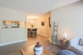 This single-floor residence at 200 Red Cedar Ct in Chesapeake, Virginia offers a well-organized layout with distinct living spaces connected by a cohesive design aesthetic. The living room serves as the centerpiece, featuring durable wood-style flooring, a textured ceiling, and a sliding glass door that opens to a private outdoor balcony, allowing natural light to fill the space and providing views of the surrounding greenery. The kitchen is accessible via a pass-through opening from the living area and is equipped with wood cabinetry, light countertops, and a gas range with an overhead vent hood. Adjacent to the kitchen, the dining area offers an intimate setting accented by a chandelier overhead and chair rail molding along the walls, adding a classic architectural detail. The bedroom is generously proportioned, featuring plush carpeting, multiple windows with sheer curtains, and ample space for large furniture. The bathroom includes a wood-toned vanity with an integrated sink, a large mirror, and a tub-shower combination. Throughout the residence, warm neutral tones on the walls create a consistent and inviting ambiance, while the transition between wood-style flooring in the main areas and carpet in the bedroom adds comfort and variety to the overall living experience.