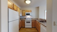Located at 1200 Elm St in Manchester, New Hampshire, this single-floor residence offers a thoughtfully laid-out interior with a variety of comfortable living spaces. The kitchen is efficiently designed in a U-shaped configuration, featuring warm honey-toned wood cabinetry, laminate countertops, and wood-look flooring. White appliances including a refrigerator, electric range, over-the-range microwave, and dishwasher are all included, providing a fully equipped cooking space. The living area is bright and open, highlighted by large sliding windows that bring in abundant natural light and offer views of the surrounding urban streetscape. Wood-look flooring extends throughout the main living space, contributing to a clean and cohesive aesthetic. The bedrooms are generously sized and finished with plush carpeting, offering a comfortable retreat. One bedroom features a double-door closet, providing ample storage. The bathrooms are finished with wood-look flooring, and one includes a vanity with a lighted mirror and a full tub-shower combination. A secondary bathroom features a clean, minimal layout with accessibility-conscious fixtures. Neutral wall tones throughout the residence create a versatile backdrop, lending a calm and inviting ambiance to the entire space.
