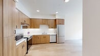 Located at 900 Chestnut St in Redwood City, CA, this efficiently designed one-bedroom, one-bathroom residence offers a clean, modern aesthetic throughout its single floor. Light hardwood flooring runs continuously across all rooms, creating a cohesive and airy feel.

The kitchen is a standout feature, outfitted with warm wood cabinetry extending floor to ceiling, stainless steel appliances including a refrigerator, range, dishwasher, and microwave, as well as white countertops and recessed lighting. The layout maximizes storage and functionality within a well-organized footprint.

The bedroom is a bright, comfortable space benefiting from a window that invites natural light and views of the surrounding neighborhood. The clean white walls and wood flooring give the room a calm, neutral atmosphere.

The bathroom is thoughtfully designed with accessibility in mind, featuring a soaking tub with a handheld showerhead, built-in grab bars, and open shelving — combining practicality with a clean, contemporary finish.

The living area is open and flexible, connecting seamlessly to the kitchen and bedroom through a simple, efficient layout. Throughout the residence, the consistent use of light tones, recessed lighting, and quality finishes contributes to a modern and welcoming ambiance.