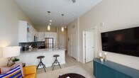 Located at 492 N Patterson Ave in Winston-Salem, NC, this single-floor residence offers a thoughtfully designed open-concept layout that seamlessly connects the kitchen, dining, and living areas. The kitchen is a standout feature, equipped with stainless steel appliances, including a refrigerator, range, and microwave. White upper cabinetry contrasts with darker lower cabinets, complemented by granite countertops and a linear tile backsplash. A peninsula with bar seating provides a casual dining option, while pendant lighting adds a contemporary touch. The living area benefits from tall ceilings and large windows with access to an outdoor space, allowing abundant natural light to fill the room. Light wood-look flooring runs throughout, contributing to the bright and airy ambiance. The bedroom is a comfortable retreat with a ceiling fan, a well-sized window that invites natural light, and neutral wall tones. The adjacent bathroom features a granite-topped vanity with dark cabinetry, a large mirror, a shower-tub combination, and light flooring that mirrors the rest of the unit, creating a cohesive and polished finish throughout.