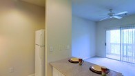 Located at 400 Stone Lion Dr in Durham, North Carolina, this single-floor residence offers a thoughtfully designed layout that maximizes comfort and functionality. The kitchen is a central highlight, featuring a peninsula-style counter with a speckled granite-look surface — ideal for casual dining or meal prep. White cabinetry and a full-size refrigerator complement the clean, light-filled aesthetic of the space. The kitchen opens directly into the adjoining living area, creating a seamless, connected flow between the two spaces. The living area is finished with plush carpeting and benefits from soft, diffused natural light that enhances the airy ambiance. Neutral wall tones throughout the home — ranging from warm beige in the kitchen to cool, light blue in the living area — create a calming and welcoming atmosphere. Ceiling fans provide efficient climate control and add to the overall comfort of the interior. The open-concept design between the kitchen and living areas makes the home feel expansive and well-suited for both everyday living and entertaining. Clean lines, practical finishes, and a cohesive color palette define the overall character of this Durham residence.
