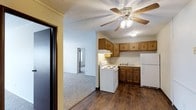 This classic 2-bedroom, 2-bathroom single-floor residence offers a practical and comfortable layout designed for everyday living. The kitchen is equipped with warm wood cabinetry, a white electric range, a double sink, and a full-size refrigerator. Dark hardwood-style flooring anchors the kitchen space, providing a rich contrast to the lighter walls and cabinetry. A ceiling fan with an integrated light fixture adds both function and a traditional aesthetic to the area. The kitchen flows naturally into the adjoining living areas, which feature plush wall-to-wall carpeting that adds warmth and comfort underfoot. A textured ceiling throughout the home contributes to the classic character of the space. The open sightlines between the kitchen and the living and hallway areas create a connected, easy-to-navigate floor plan. Natural light filters in through windows visible in the adjoining rooms, brightening the interior. The traditional design elements, including the wood-toned cabinetry and neutral color palette, give this home a timeless, welcoming ambiance suited to a range of lifestyles.