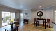 Located at 1802 Ennis Joslin Rd in Corpus Christi, Texas, this single-floor residence offers a well-appointed and cohesive living environment with a neutral, contemporary aesthetic throughout. The open-concept living and dining area is anchored by warm wood-look flooring, crown molding, and soft gray walls that create an inviting and airy atmosphere. The living room features sliding glass doors that open to a private balcony, filling the space with natural light and providing outdoor views. Adjacent to the living area, the dining space is defined by a dark wood table paired with woven chairs, accented by a distinctive round mirror. The kitchen is efficiently designed with white cabinetry, dark granite-style countertops, a breakfast bar peninsula, and a full suite of stainless steel appliances including a refrigerator, electric range, and microwave. The bedroom offers a comfortable retreat with ample natural light from large windows fitted with horizontal blinds, a ceiling fan, and access to a closet. The bathroom includes white cabinetry, a framed mirror, and a light-toned countertop vanity. The consistent flooring and cohesive color palette tie each area of this well-designed single-floor residence together seamlessly.