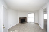 This single-floor residence offers a well-organized layout designed for comfortable everyday living. The living room serves as the heart of the home, anchored by a classic brick wood-burning fireplace with a raised hearth. Neutral-toned carpet extends throughout the space, and a sliding glass door fills the room with natural light while providing access to an outdoor balcony or patio area.

The galley-style kitchen is efficiently designed with dark wood cabinetry lining both walls, offering generous upper and lower storage. Light wood-toned laminate countertops run continuously along the workspace, complemented by a stainless steel sink, a white refrigerator, a white dishwasher, and a coil-top electric range with overhead ventilation. Light-toned tile flooring adds a practical, easy-clean surface throughout the kitchen.

The bedrooms are carpeted and bright, each featuring windows that allow natural light to filter in. Each room is equipped with a dedicated closet, providing ample storage. The primary bedroom includes a particularly spacious walk-in closet with built-in shelving and hanging rods. The adjoining bathroom features a single-basin vanity with dark wood cabinetry and a large wall mirror. Textured ceilings are consistent throughout the home, contributing to its classic residential character.