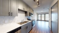 This contemporary single-floor residence offers a thoughtfully designed layout with clean, modern finishes throughout. The kitchen is a standout feature, showcasing gray shaker-style cabinetry with matte black hardware, crisp white quartz countertops, and a striking herringbone marble tile backsplash. Stainless steel appliances — including an electric range, over-the-range microwave, and dishwasher — complete the functional yet elegant cooking space. Track lighting overhead highlights the kitchen's refined details.

The kitchen flows seamlessly into an open living area, where rich hardwood-style flooring extends throughout and large French-style doors flood the space with natural light while providing access to the outdoors. Recessed lighting and neutral walls create a bright, welcoming atmosphere well-suited for a variety of furniture arrangements.

The bedroom offers generous storage with dual closets, one of which features built-in hanging rods. Consistent gray-toned door frames and trim carry the modern palette throughout. The bathroom is finished with matching gray cabinetry, a white countertop vanity, a framed mirror, and hardwood-style flooring, maintaining the cohesive aesthetic found across the entire residence. Every detail of this space reflects a commitment to contemporary, functional living.