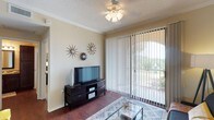 This single-floor residence offers a comfortable and functional layout with thoughtfully designed living spaces throughout. The living room serves as a welcoming focal point, featuring rich hardwood-style flooring, crown molding, a ceiling fan with light fixture, and a large sliding glass door with vertical blinds that invites natural light and provides views of the surrounding greenery outside.

The open-concept layout connects the living area to a cozy dining nook, which is accented by a full-length mirrored wall that enhances the sense of space and light. The kitchen is well-equipped with dark espresso cabinetry, granite countertops, a stainless steel refrigerator, black appliances including an electric range with overhead microwave, and a stainless steel sink — with access to a laundry or utility area just off the kitchen.

Both bedrooms are generously proportioned, each featuring carpet flooring, ceiling fans, crown molding, and ample natural light from large windows with draping curtains. One bedroom includes a spacious walk-in closet with wire shelving, while the other provides convenient access to an adjacent bathroom. The bathrooms are finished with granite-topped vanities, dark wood cabinetry, large framed mirrors, and a tub-shower combination. Throughout the unit, warm neutral tones create a cohesive and inviting ambiance.