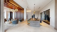 Located at 15 Artisan in Salem, New Hampshire, this refined single-floor amenity space presents an impressive blend of modern luxury and thoughtful design across a generously proportioned floor plan. The entrance hallway sets an immediate tone of sophistication, featuring marble-clad walls, large-format tile flooring, and a sculptural wood bench that doubles as a striking art piece.

The central lounge area commands attention with dramatic spherical chandelier clusters suspended from high ceilings, warm wood slat wall panels, and a curated seating arrangement of curved, contemporary chairs that invites relaxed conversation. A statement fireplace wall, clad in textured stone and topped with a mounted display, anchors one end of the living area, while floor-to-ceiling windows flood the space with natural light and outdoor views.

The kitchen area is equally refined, featuring an extended island with crisp white countertops, warm wood cabinetry, and an eye-catching geometric mosaic tile backsplash. Sleek pendant lighting and expansive windows further elevate this functional yet stylish space.

The dining and conference area showcases a substantial wood-topped table with contemporary seating beneath an artistic wire chandelier, seamlessly flowing into the reception zone. Throughout, a cohesive palette of stone, warm wood tones, and brushed gold accents creates a welcoming, upscale ambiance ideal for community gathering.