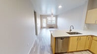 Located at Orenco Station in Hillsboro, Oregon, this single-floor unit offers a clean, contemporary design with an efficient and well-considered layout. Light-toned luxury vinyl plank flooring runs throughout the living areas, complementing the bright white walls and creating a cohesive, modern aesthetic.

The open-concept kitchen flows seamlessly into the living area, making it ideal for everyday living. The kitchen is outfitted with light maple cabinetry, a subway tile backsplash, quartz countertops, and a full suite of stainless steel appliances including an electric range, over-the-range microwave, refrigerator, and dishwasher. A peninsula with an undermount sink adds additional workspace and separates the kitchen from the living space.

The living area is generously proportioned, featuring a ceiling fan, a wall-mounted HVAC unit, and a glass door that opens to a private balcony with views of the surrounding building exterior, allowing natural light to fill the room.

The bathroom features light maple vanity cabinetry with a quartz countertop, a full soaking tub and shower combination with built-in shelving, and light wood-look flooring that ties the space together with the rest of the unit.