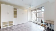 Located in Portland's vibrant NW district, this efficiently designed studio offers a smart, modern layout that makes excellent use of its compact footprint. The main living area features light gray hardwood-style flooring, crisp white walls, and a ceiling fan overhead. A large, multi-pane window floods the space with natural light while framing views of the surrounding neighborhood. Built-in white cabinetry with integrated open shelving provides generous storage, complemented by a fold-away murphy bed that maximizes the flexibility of the living area. A wall-mounted desk with a wood-top surface offers a dedicated workspace beside the window. The kitchen is thoughtfully equipped with stainless steel appliances, including a full-size refrigerator, dishwasher, and built-in microwave, alongside white upper cabinetry, light-toned lower drawers, a smooth cooktop, and a single-basin sink with a modern faucet. The bathroom includes a shower/tub combination with chrome fixtures and a grab bar, finished with wood-look vinyl flooring and clean white walls throughout. The overall aesthetic is clean, contemporary, and functional — well-suited for efficient urban living in the heart of Portland.