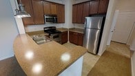 This single-floor space showcases a well-appointed kitchen designed for both functionality and everyday comfort. The kitchen is outfitted with a full suite of stainless steel appliances, including a refrigerator, a gas range with oven, and an over-the-range microwave, all contributing to a cohesive, modern aesthetic. Rich, medium-toned wood cabinetry lines the walls, offering generous upper and lower storage solutions throughout the space. The cabinetry's warm hue is complemented by stone-toned countertops that extend across the workspace, including a peninsula-style counter that provides additional prep area and casual seating potential. A stainless steel sink with a single-handle faucet is integrated into the countertop, adding a practical and polished touch. The flooring consists of neutral-toned tile, which ties together the warm wood and metallic finishes harmoniously. The layout follows a functional U-shaped configuration, maximizing workspace efficiency while maintaining an open, accessible feel. Overall, the kitchen presents a well-organized and inviting environment suited for daily use.