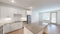 Located at 2001 Plateau Vista Blvd in Round Rock, TX, this single-story, one-bedroom unit offers a well-designed open-concept floor plan that maximizes its compact footprint. The kitchen is a standout feature, boasting crisp white shaker-style cabinetry, a classic subway tile backsplash, quartz countertops, and a full suite of stainless steel appliances including a refrigerator, dishwasher, microwave, and range. A central kitchen island provides additional prep and counter space, seamlessly connecting the kitchen to the living area.

The living space is bright and airy, with light-toned wood-style flooring flowing throughout and multiple windows fitted with blinds that allow ample natural light while maintaining privacy. A glass-paneled door in the living area provides access to the outdoors. The bedroom is a comfortable size, equipped with a ceiling fan, a dedicated closet, and an attached bathroom, offering a practical and private retreat. The clean white walls and neutral color palette throughout create a modern, cohesive aesthetic. The overall ambiance is clean, contemporary, and functional, making efficient use of every square foot.