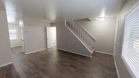 This two-story residence offers a practical and well-appointed layout across two levels. The main floor features a spacious living area finished with dark hardwood-style flooring and neutral gray walls, creating a clean, contemporary aesthetic. A white-railed staircase connects the floors and adds a crisp architectural detail to the space. A convenient half bathroom is accessible on the main level.

The kitchen is well-equipped with stainless steel appliances, including a refrigerator, electric range, and dishwasher. White cabinetry provides ample storage, while light speckled countertops and a double-basin sink complement the overall design. Natural light enters through multiple windows throughout the home.

Upstairs, two generously sized bedrooms are finished with plush carpet and feature ceiling fans with integrated lighting. The primary bedroom includes access to a walk-in closet and an adjoining full bathroom. The full bathroom is equipped with a tub-shower combination, wood-style flooring, and a vanity with speckled countertops. Both bathrooms share a consistent design aesthetic, reinforcing the home's cohesive, move-in-ready presentation.