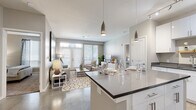 Located at 801 NW Tenth St in Oklahoma City's vibrant midtown district, this single-floor residence showcases a thoughtfully designed open-concept layout with modern finishes throughout. The kitchen is a standout feature, equipped with crisp white cabinetry, dark countertops, black appliances, track lighting, and a large center island with bar seating — all illuminated by elegant pendant lights. Polished concrete floors flow seamlessly from the kitchen into the expansive living and dining area, where French doors flood the space with natural light and provide outdoor access. The living room offers a welcoming atmosphere, highlighted by large windows with plantation-style blinds, generous wall space for artwork, and an open feel that encourages comfortable living. The bedroom is a serene retreat, featuring plush carpet, large windows with sheer curtains, and ample room for furnishings. The bathroom includes a full soaking tub framed by floor-to-ceiling stone-look tile, while an additional bathroom features white cabinetry with dark countertops, a large mirror, and direct access to a walk-in closet. Neutral tones, clean lines, and contemporary design elements define the overall ambiance of this well-appointed residence.