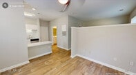 This efficiently designed one-bedroom, one-bathroom unit maximizes its compact footprint through a thoughtful open layout. Wood-look plank flooring runs consistently throughout the entire space, lending a cohesive and clean aesthetic. The combined kitchen and living area forms the heart of the unit, where a galley-style kitchen is outfitted with stainless steel appliances — including a refrigerator, electric range, microwave, and dishwasher — complemented by white cabinetry and light stone-finish countertops. A peninsula breakfast bar provides additional counter space and defines the transition between the kitchen and the open living area. The living room benefits from a sliding glass door fitted with vertical blinds, introducing natural light and outdoor views. A half-wall partition adds subtle architectural definition to the space without compromising openness. The bedroom is a well-proportioned private retreat featuring a large window that allows ample natural light and views of surrounding greenery. The bathroom is finished with a white vanity, stone-finish countertop, a tub-shower combination with tile surround, and matching wood-look flooring. A dedicated closet provides practical storage. Neutral gray walls throughout contribute to a bright, modern ambiance.
