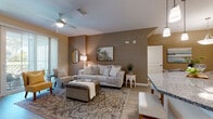 Located at 3654 Island Club Dr in North Port, Florida, this single-story residence offers a thoughtfully designed open-concept floor plan that promotes a seamless flow between living spaces. Light wood-style flooring runs throughout the main areas, complementing a warm, neutral color palette accented by taupe feature walls that add depth and visual interest.

The living area is generously proportioned, featuring vaulted ceilings, a ceiling fan, and a sliding glass door that draws in natural light. The space connects directly to a dedicated dining area, which benefits from its own pendant lighting and direct sightlines to the kitchen. A defined entry foyer with transom window provides a welcoming arrival point.

The kitchen is well-equipped with rich dark wood cabinetry, granite countertops, a substantial breakfast bar peninsula with bar seating, and a full suite of stainless steel appliances including a refrigerator, electric range, and microwave. An in-unit laundry area is accessible directly from the kitchen corridor.

The bedroom features plush carpeting, a large window with natural light, and a relaxed, airy ambiance. The bathroom includes a dark wood vanity, open shelving, and wood-look tile flooring, maintaining the cohesive design aesthetic found throughout the residence.