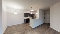 This single-story residence at Ashton Park offers a well-designed open-concept layout that seamlessly connects the kitchen, dining, and living areas. The kitchen is a standout feature, showcasing rich dark cabinetry paired with light granite countertops and a classic subway tile backsplash. Stainless steel appliances, including a refrigerator, range, and microwave, provide a modern, functional workspace. A peninsula with pendant lighting above extends the counter space and serves as a natural dividing point between the kitchen and the main living area.

The living area is generously proportioned, with dark wood-style flooring running throughout the main spaces, adding warmth and visual continuity. A ceiling fan overhead and a glass-paneled door leading to an outdoor area bring in natural light and enhance the sense of openness. Pendant and bowl-style light fixtures contribute to the overall contemporary aesthetic.

The bedrooms feature plush carpeting and windows fitted with blinds, allowing for adjustable natural light. The rooms offer comfortable proportions with clean, neutral walls suited to a variety of furnishing styles. Additional utility spaces, including a laundry area and electrical panel access, are conveniently integrated into the layout, rounding out a practical and cohesive living environment.