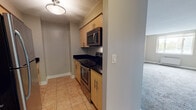 Situated at 1450 Washington Blvd in Stamford, Connecticut, this single-floor residence offers a well-organized layout designed for comfortable everyday living. The kitchen is outfitted with light wood cabinetry featuring sleek bar-pull hardware, dark granite countertops, and stainless steel appliances including an electric range and an over-the-range microwave. The tile flooring in the kitchen and entry hallway provides a clean, durable transition into the living areas. The main living space is generously proportioned, featuring neutral-toned carpet, soft beige walls, and a large window that allows natural light to fill the room while offering views of the surrounding Stamford cityscape. A wall-mounted heating unit ensures year-round comfort. The bedroom is a well-sized, carpeted room with its own closet fitted with a full-width rod and shelving, providing ample storage. The bathroom is finished with tile flooring, a light wood vanity with a white countertop, a large mirror with overhead lighting, and white subway tile accents. Throughout the space, the consistent use of neutral tones and practical finishes creates a clean, functional, and move-in-ready environment in a prime Stamford location.