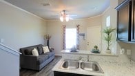 This two-floor space showcases a thoughtfully designed open-concept layout where the kitchen flows seamlessly into the living area. The kitchen is equipped with granite-style countertops, a double stainless steel sink, and ample counter space, making it both functional and visually appealing. The living area comfortably accommodates seating and is highlighted by warm, neutral-toned walls that create an inviting atmosphere. Crown molding adds a refined architectural detail throughout the space, while a ceiling fan with integrated lighting provides both comfort and illumination. Dark hardwood-style flooring anchors the space and contrasts elegantly with the light countertops and walls. A window dressed with patterned curtains allows natural light to filter into the main living area, contributing to the bright and airy feel of the space. The open sightlines between the kitchen and living room enhance the sense of spaciousness. The second floor adds additional functional living space to this well-appointed home. Overall, the space balances practicality with modern aesthetic touches, creating a comfortable and cohesive environment.
